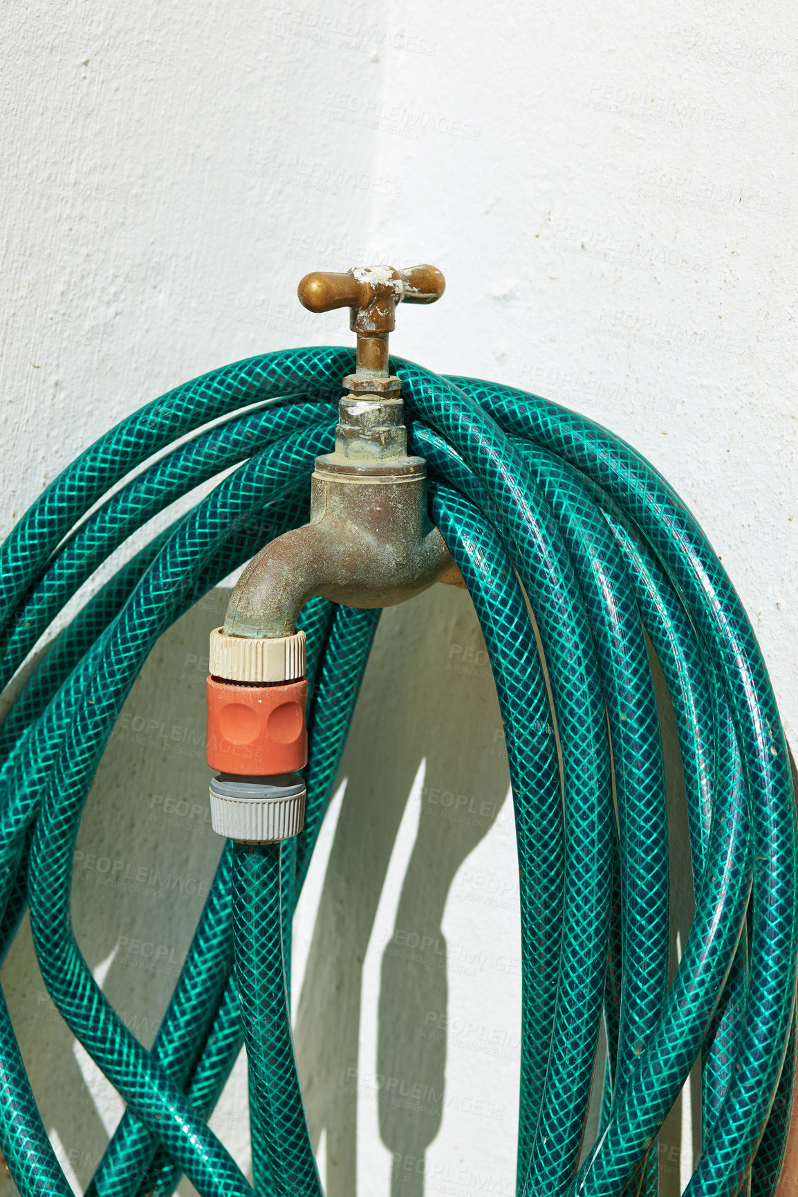 Buy stock photo Tap, pipe and garden hose with attachment for water, pressure or environmental care at home. Closeup of faucet with plastic hosepipe rolled up on wall for liquid supply, service or outdoor gardening