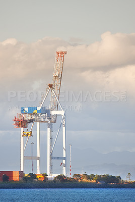 Buy stock photo A crane and shipping containers in a shipyard surrounded by the ocean. Industrial hoisting crane in a logistics or cargo harbor at a seaport for the transportation of liquid materials
