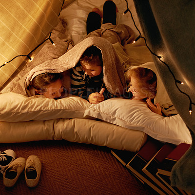 Buy stock photo Children, happy and sleepover in tent at night with conversation, bonding and holiday adventure or vacation. Young friends or kids by fairy lights, pillows and blanket at home for fun storytelling