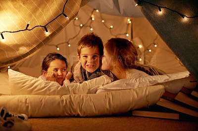 Buy stock photo Kids, happy and playing in tent at night with love, kiss and bonding for holiday adventure or vacation. Portrait of children with fairy lights, pillows and blanket at home and talk, secret or whisper