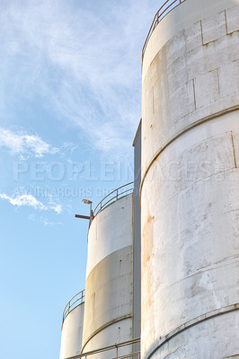 Buy stock photo Closeup, silo and tank at plant for agriculture, bulk storage and product safety with sky, clouds and outdoor. Container, agricultural structure and oil refinery tower with distillery for business