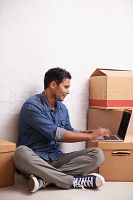 Buy stock photo A handsome young man using his laptop on the floor with boxes surrounding him