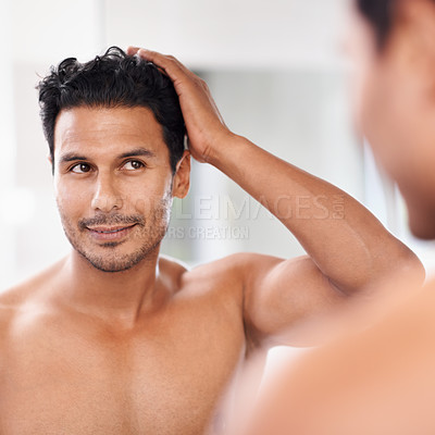 Buy stock photo A handsome young man admiring himself in the mirror