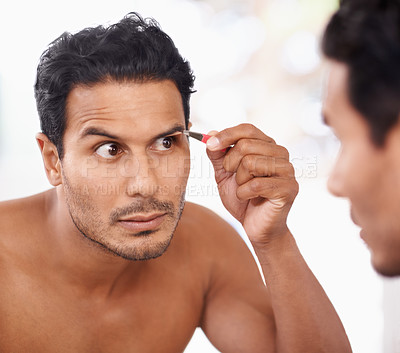 Buy stock photo A young man plucking his eyebrows while looking in the mirror