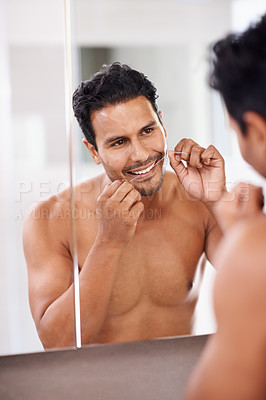 Buy stock photo A young man flossing his teeth while looking in the mirror