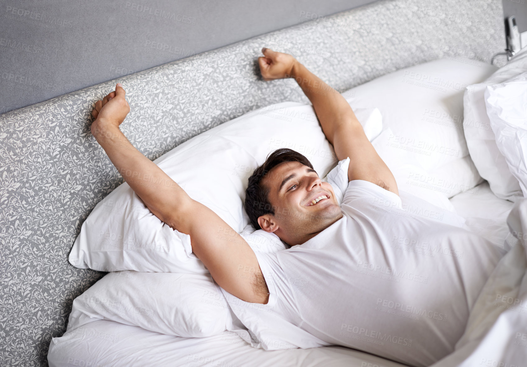 Buy stock photo Cropped shot of a young man stretching in bed while waking up