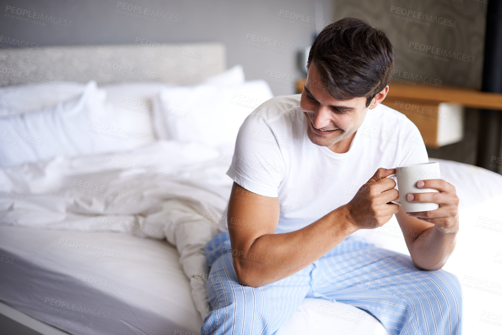Buy stock photo Cropped shot of a handsome young man drinking coffee on the edge of his bed