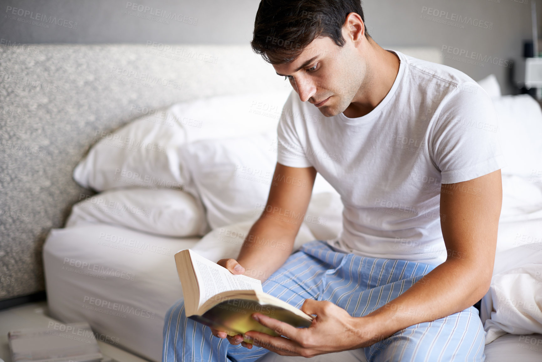 Buy stock photo Man, reading and pajamas for morning, routine and book in bedroom for wellness and literature for class. Male person, hobby and student for relaxation, leisure and novel for home free time in house