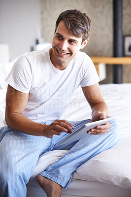 Buy stock photo Cropped shot of a handsome young man using a tablet on the edge of his bed