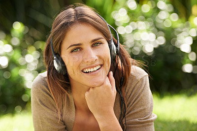 Buy stock photo Shot of a gorgeous young woman laying outdoors listening to music
