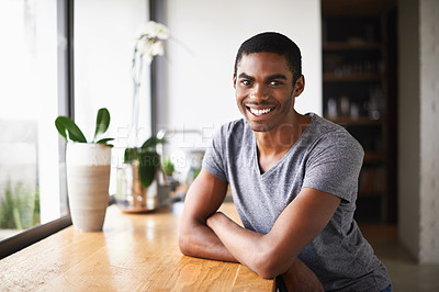 Buy stock photo Shot of an African man sitting crossed arms at a counter near a large window
