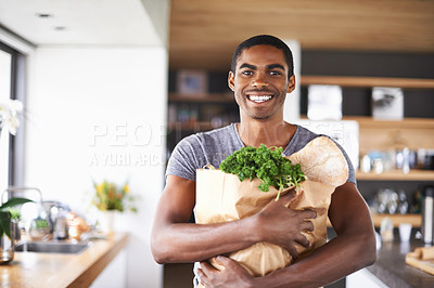 Buy stock photo Shot of a young african man holding a bag of groceries indoors