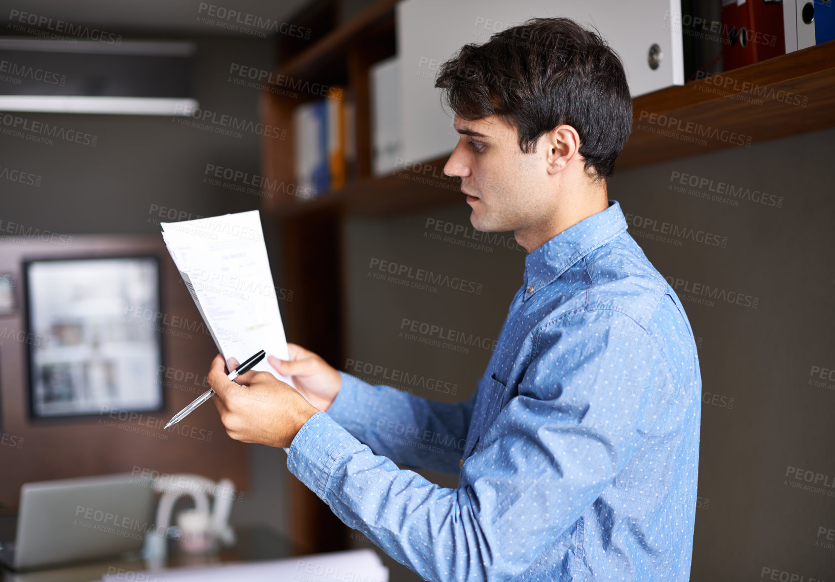 Buy stock photo Shot of a handsome young businessmen looking over some paperwork