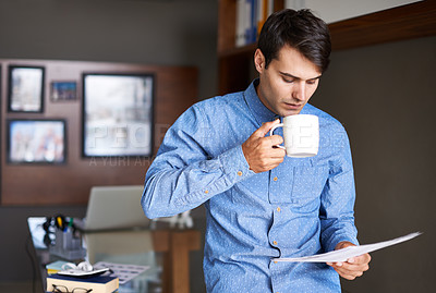 Buy stock photo A young businessman drinking coffee while going through some paperwork