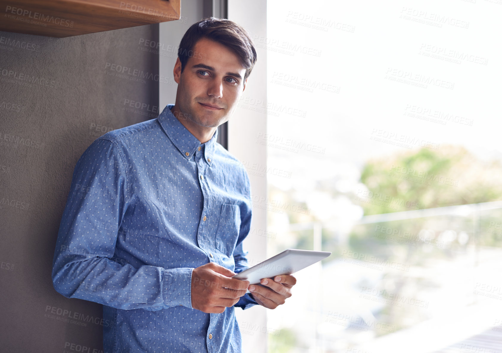 Buy stock photo Shot of a young businessman standing with a digital tablet