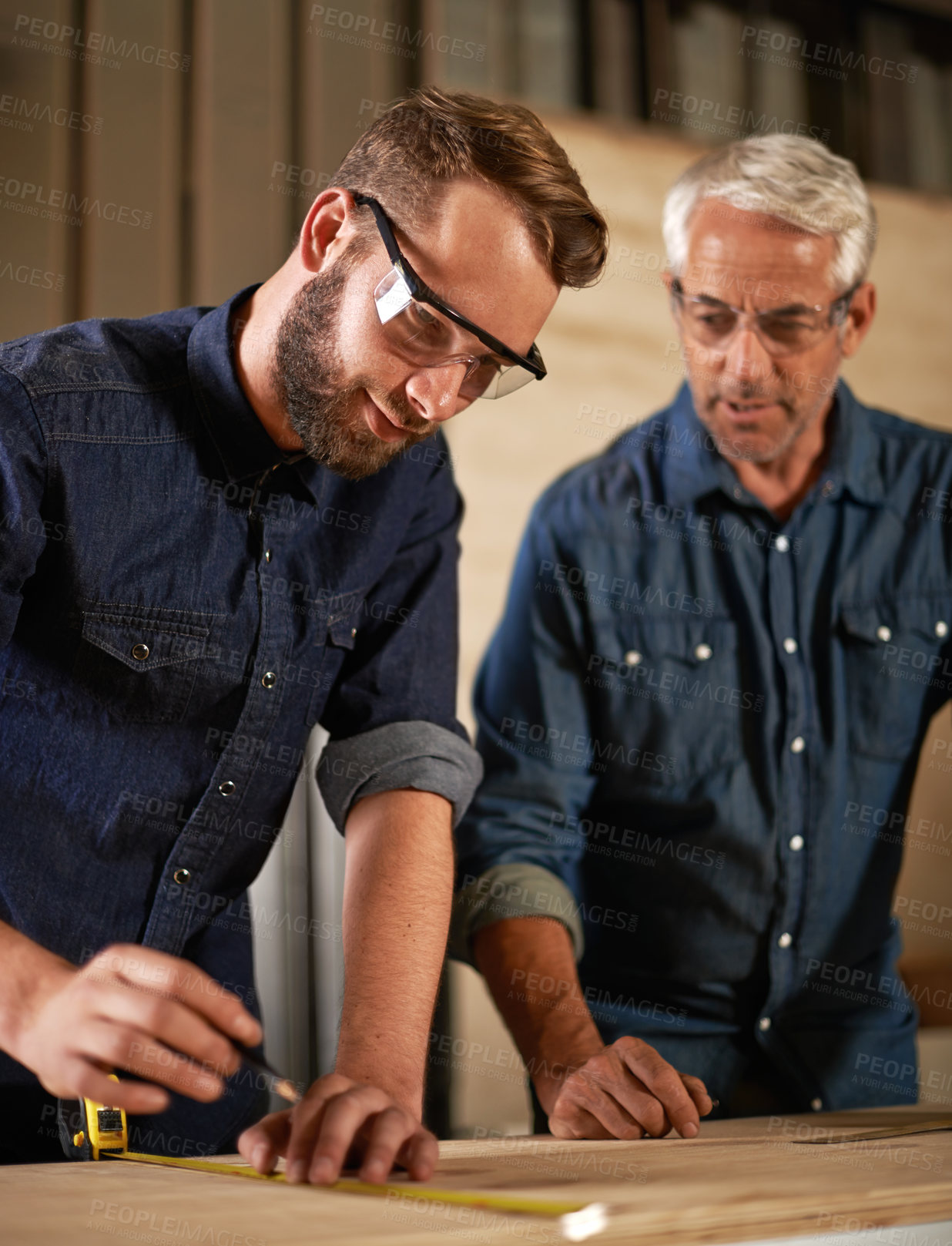 Buy stock photo Wood, learning and carpentry apprentice with mentor in designer furniture manufacturing workshop. Mentorship, senior carpenter and young man, measuring tape and focus on teaching sustainable business