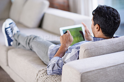Buy stock photo Cropped shot of a  young man using his tablet while relaxing at home