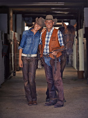 Buy stock photo Shot of a cowboy and cowgirl leading a horse out of a stable