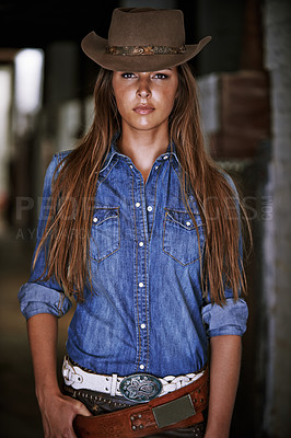 Buy stock photo An attractive young cowgirl standing in the stables 