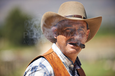 Buy stock photo Portrait, cowboy and man smoking cigar at farm in the rural countryside in Texas. Ranch, face and serious person with tobacco in western hat outdoor, nicotine and casual clothes in nature at stable
