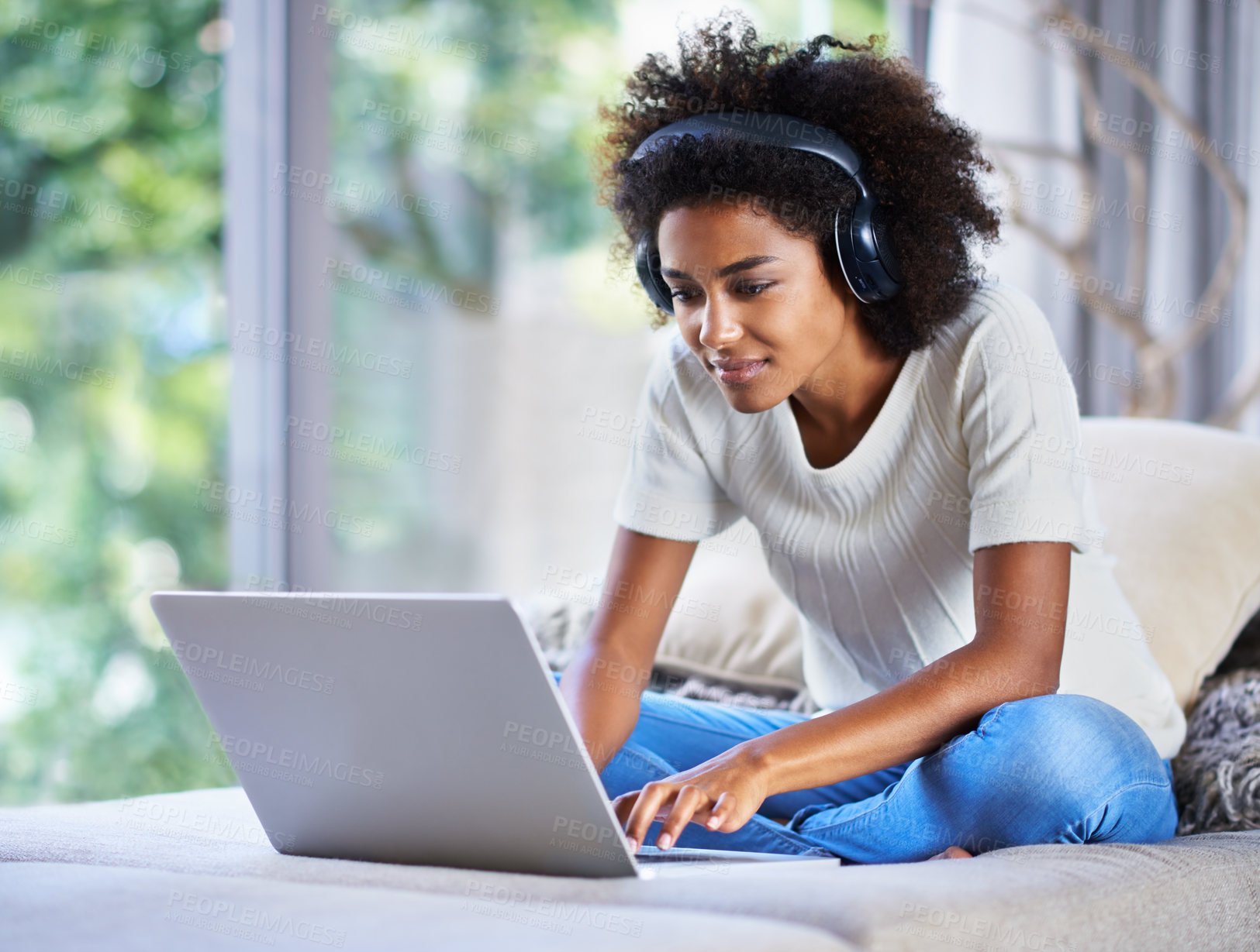 Buy stock photo Shot of a young woman sitting at home using a laptop and wearing headphones