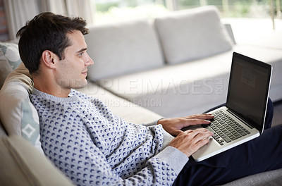 Buy stock photo Man, laptop and sofa in living room for tech, social media and research for home or indoor on weekend. Male person and smile with hand on keyboard for browse, type and screen with internet and online