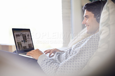 Buy stock photo Laptop, headphones and happy man in home typing, relax or listening to sound of radio podcast on sofa. Computer, music and smile of person in lounge for internet, social media and streaming audio