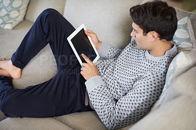 Buy stock photo Man, tablet and relax on sofa in living room for tech, social media and research in home or indoor on weekend. Male person and looking with touch on screen for browse with internet and online 