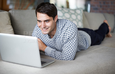 Buy stock photo Cropped shot of a young man using his laptop on his sofa