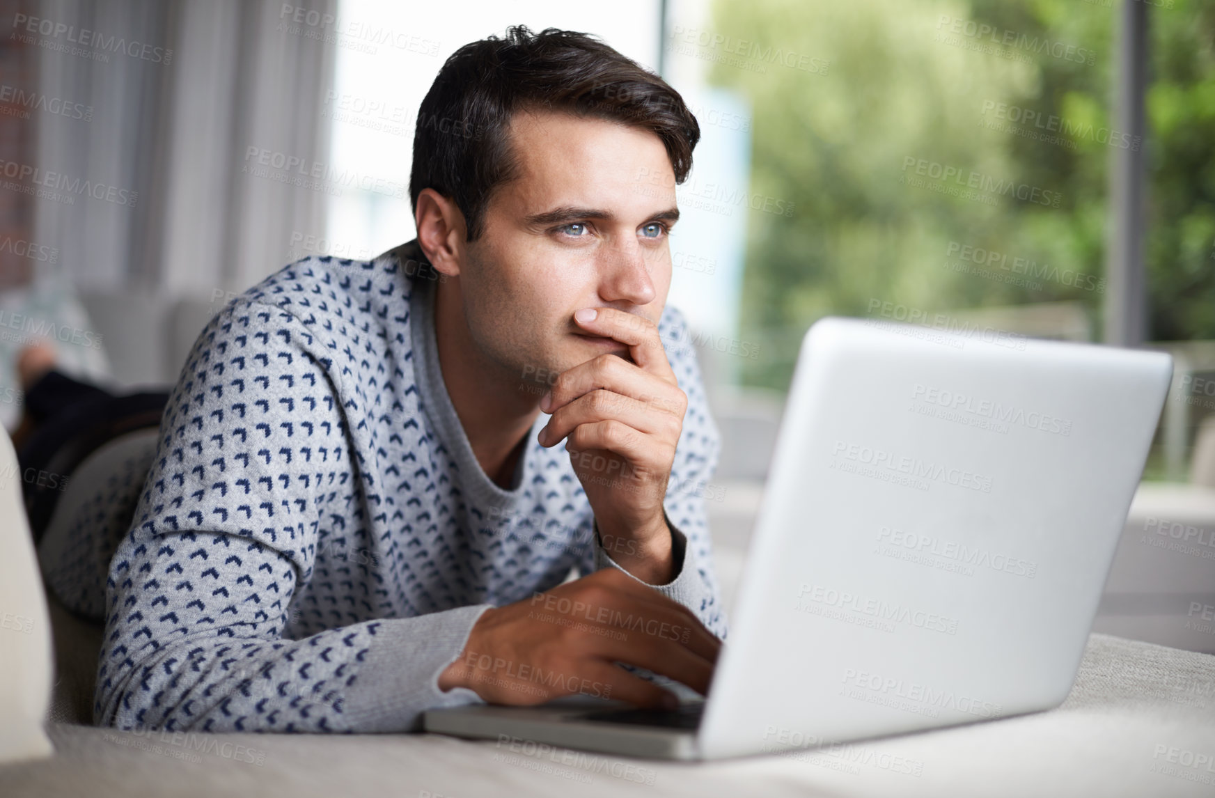 Buy stock photo Shot of a young man contemplating while using his laptop