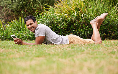Buy stock photo Shot of a handsome young man lying on the grass using a digital tablet