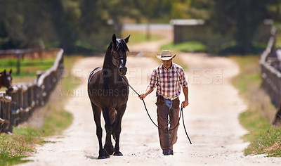 Buy stock photo Shot of a cowboy leading his horse by the reins