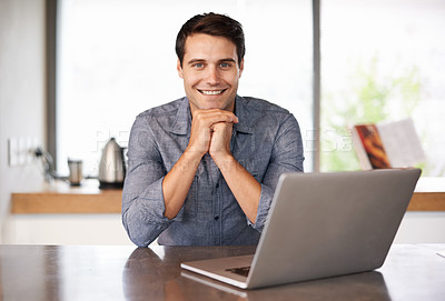 Buy stock photo Portrait of a handsome young man sitting in his kitchen with his laptop