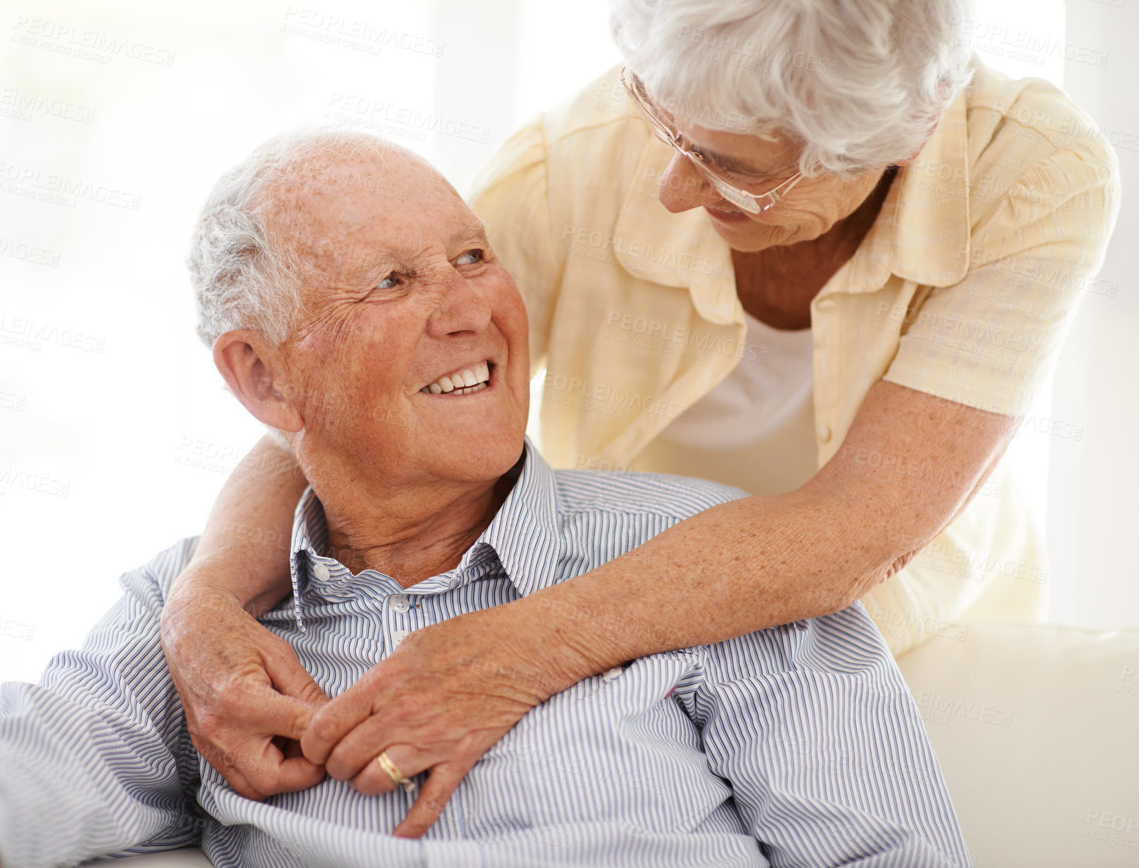 Buy stock photo Couple, senior and hug or love in looking, home and relax together for bonding and smile. Elderly people, embrace and care in marriage or relationship in retirement, couch and security in house