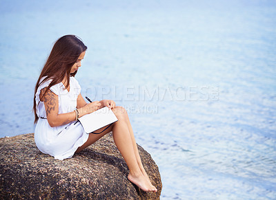 Buy stock photo Full length shot of a gorgeous tattooed young woman sitting on a rock writing in a diary