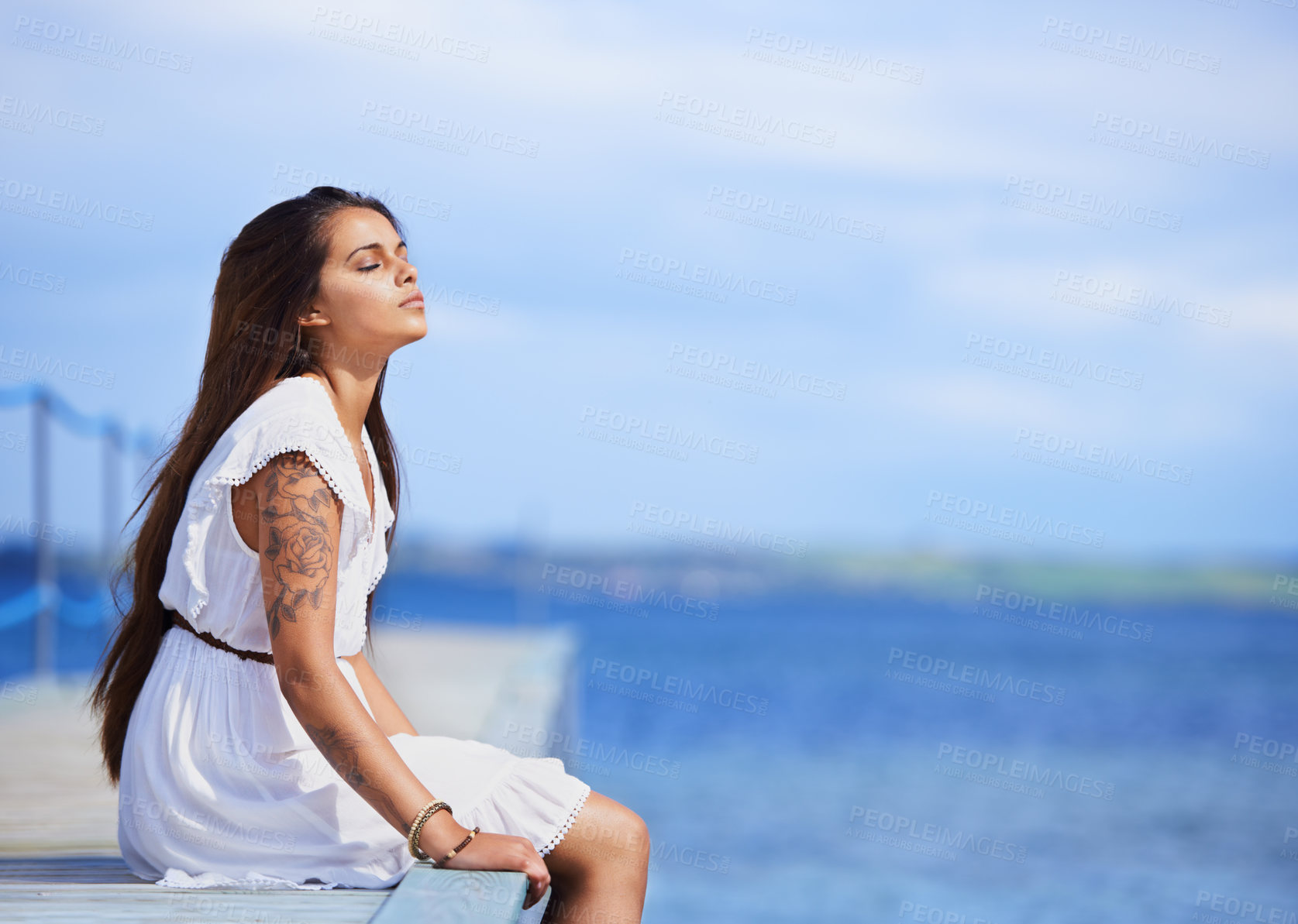 Buy stock photo Cropped shot of a gorgeous tattooed young woman sitting on a pier