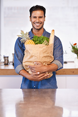 Buy stock photo Portrait of a handsome man holding a shopping bag of healthy food in his arms