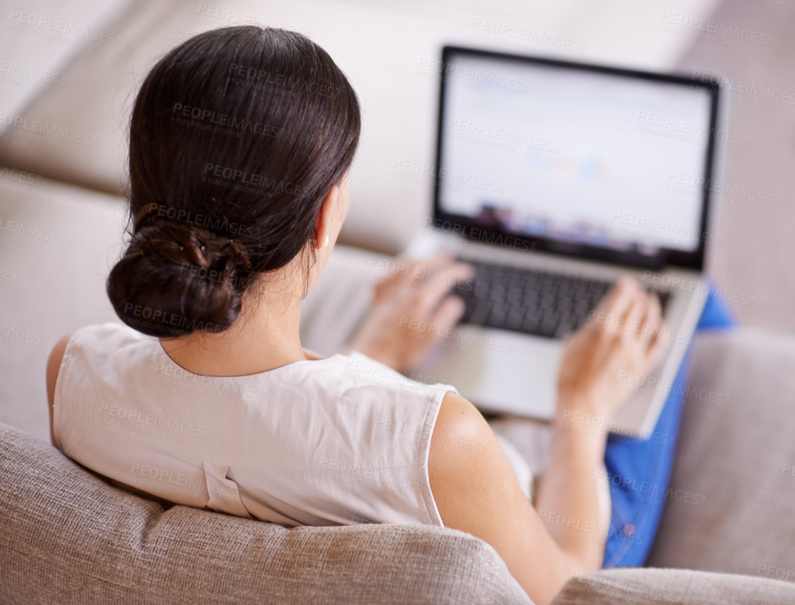 Buy stock photo Over the shoulder shot of a young woman sitting on a sofa using a laptop