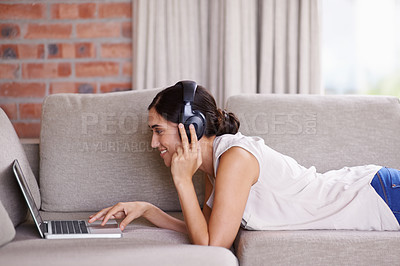 Buy stock photo Woman, laptop and lying on couch with headphones for streaming, music and search for web video in home. Girl, smile and scrolling for movie, podcast or meme on internet to relax on sofa with computer