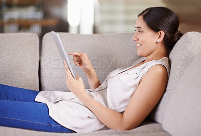 Buy stock photo Shot of a young woman lying on a sofa using a digital tablet