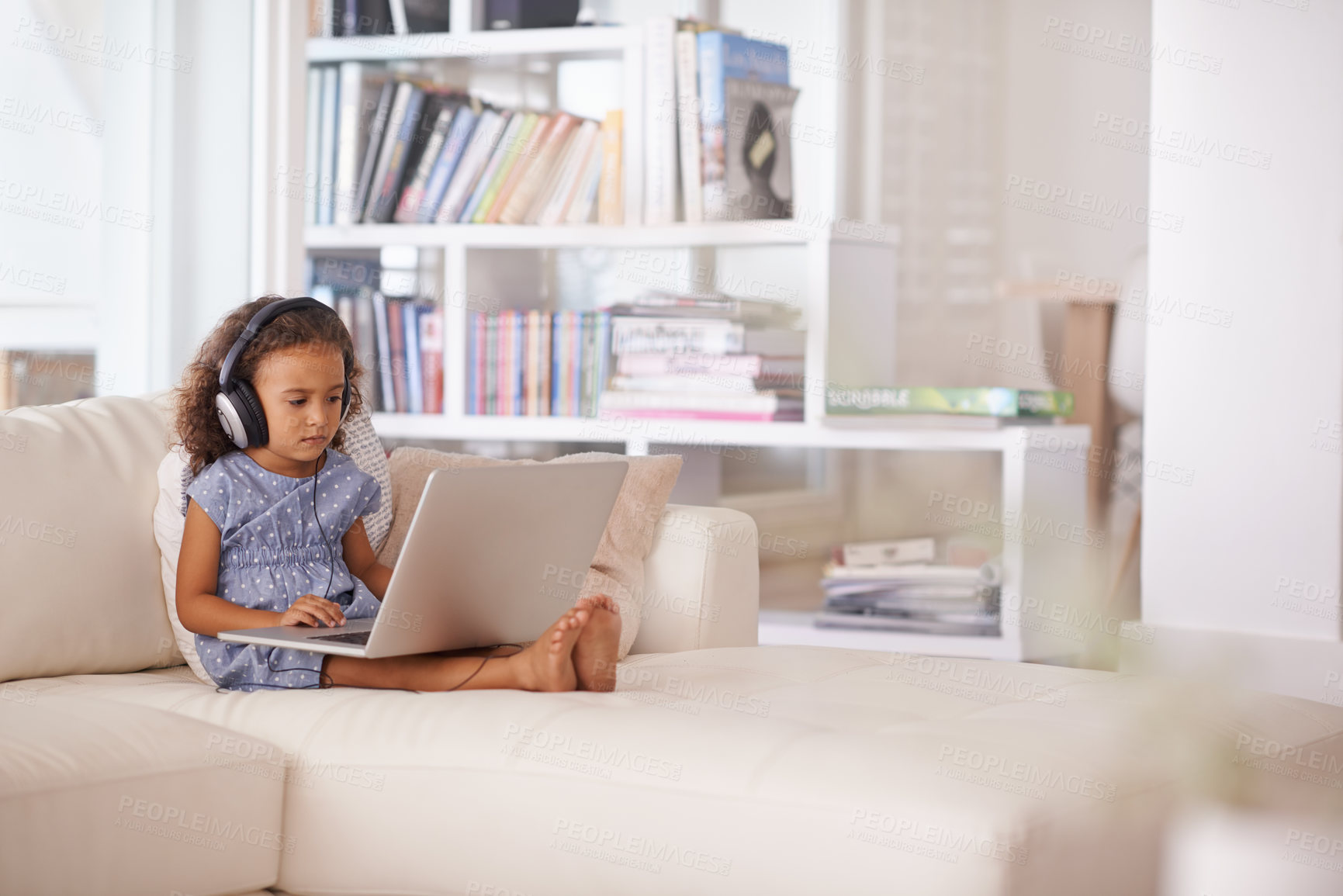 Buy stock photo Shot of a little girl using headphones and a laptop while sitting at home