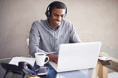 Buy stock photo Shot of a young businessman wearing a headset while working on his laptop at home