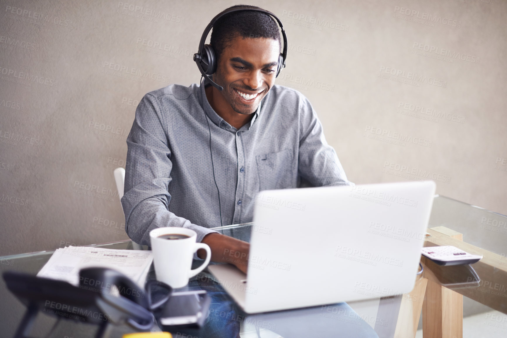 Buy stock photo Shot of a young businessman wearing a headset while working on his laptop at home