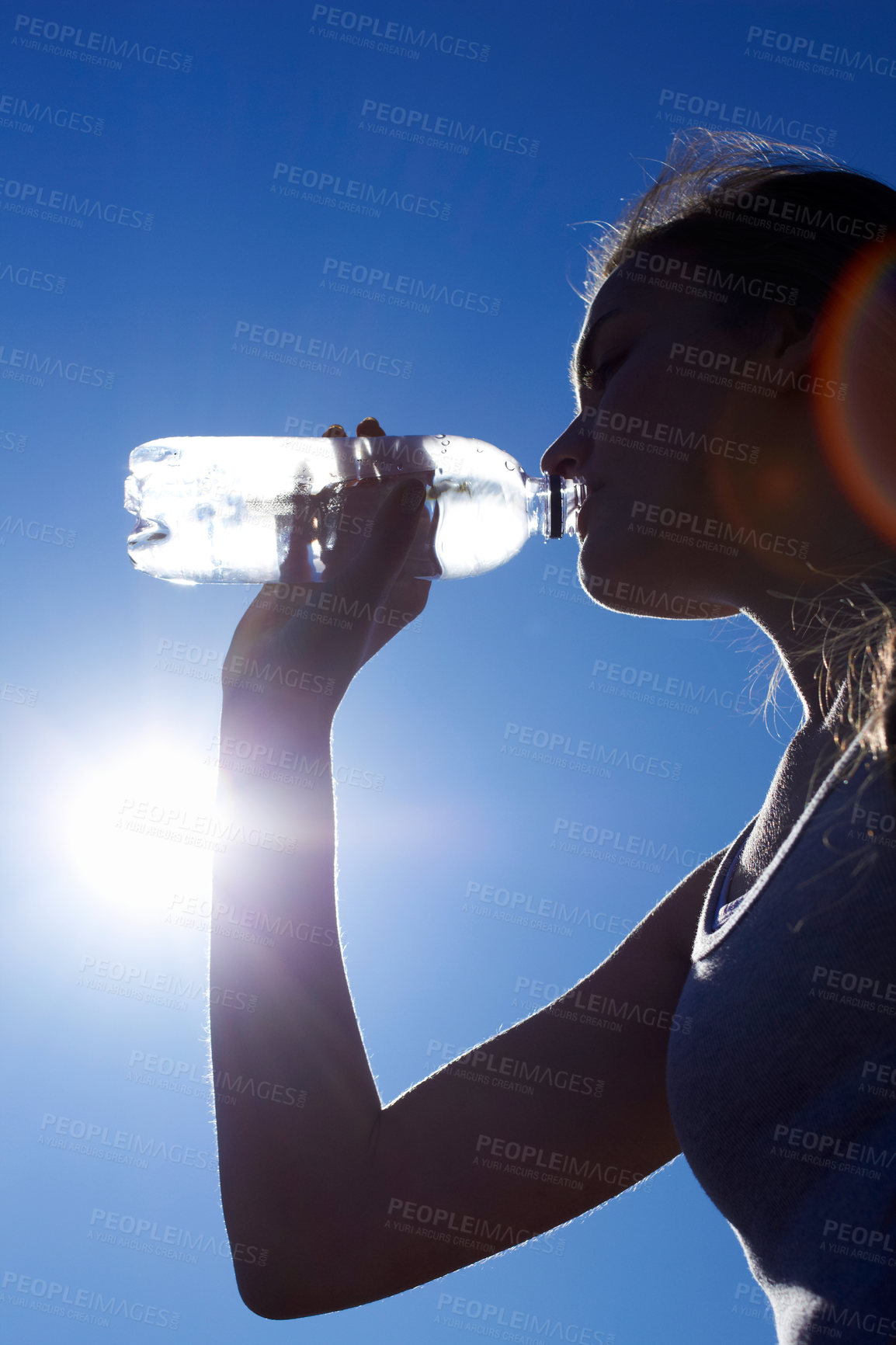 Buy stock photo Low angle silhouette shot of a woman drinking water against a blue sky