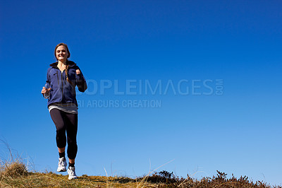 Buy stock photo A sporty young woman running along a grassy trail on a sunny day