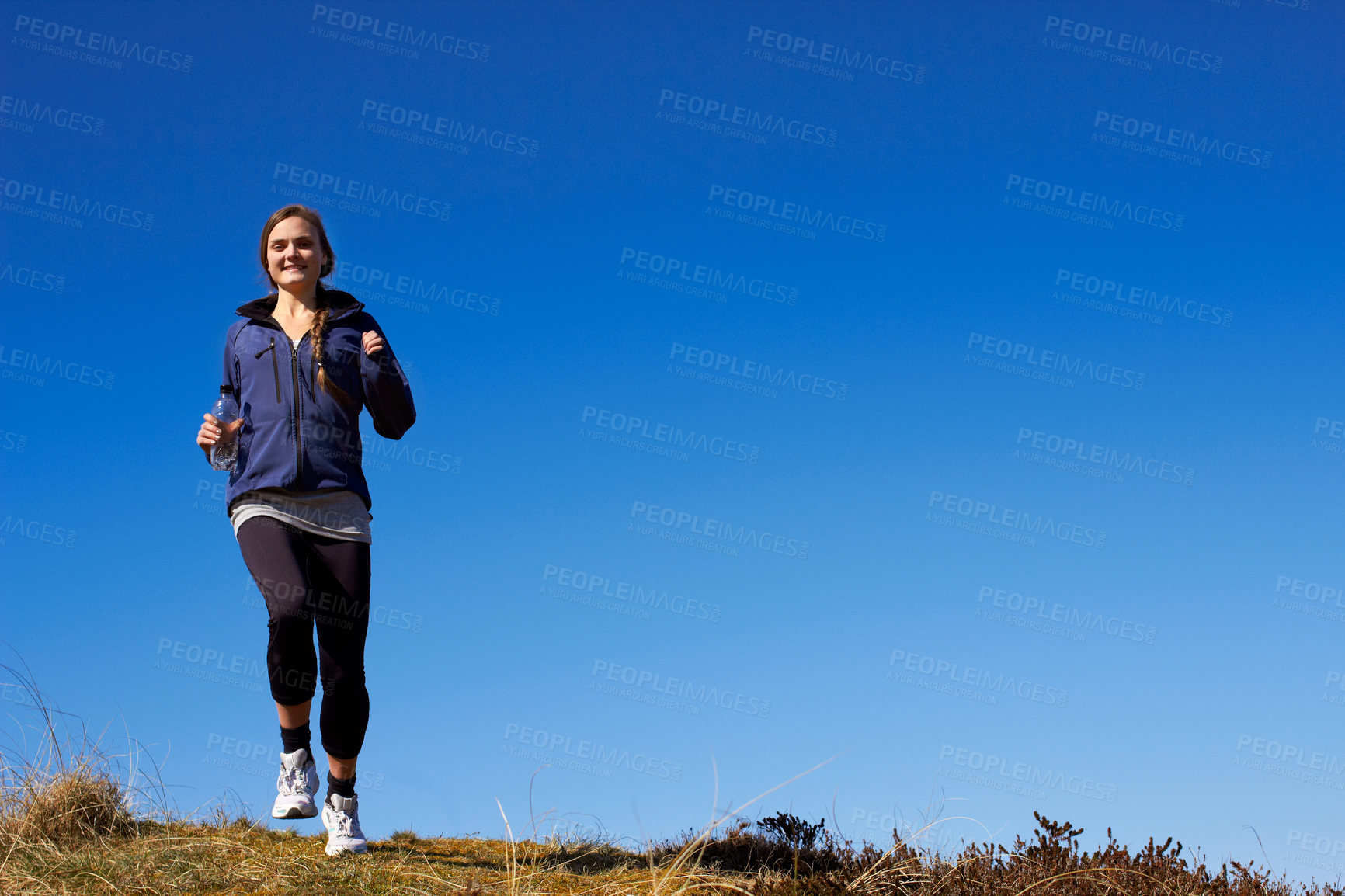 Buy stock photo A sporty young woman running along a grassy trail on a sunny day
