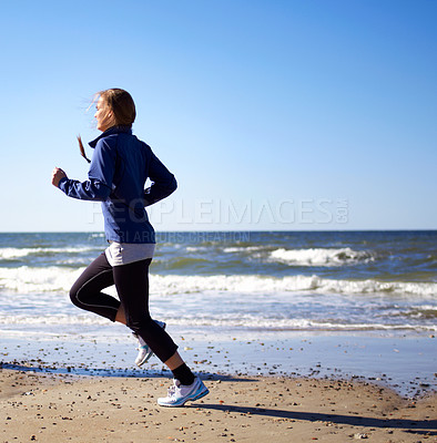 Buy stock photo A sporty young woman  running along the beach