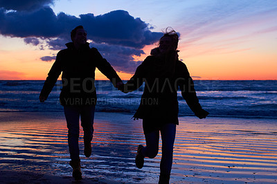 Buy stock photo Sunset, silhouette and couple running at beach on romantic date, vacation or holiday in nature. Man and woman holding hands with love and care on travel, adventure or trip with clouds, sky and ocean