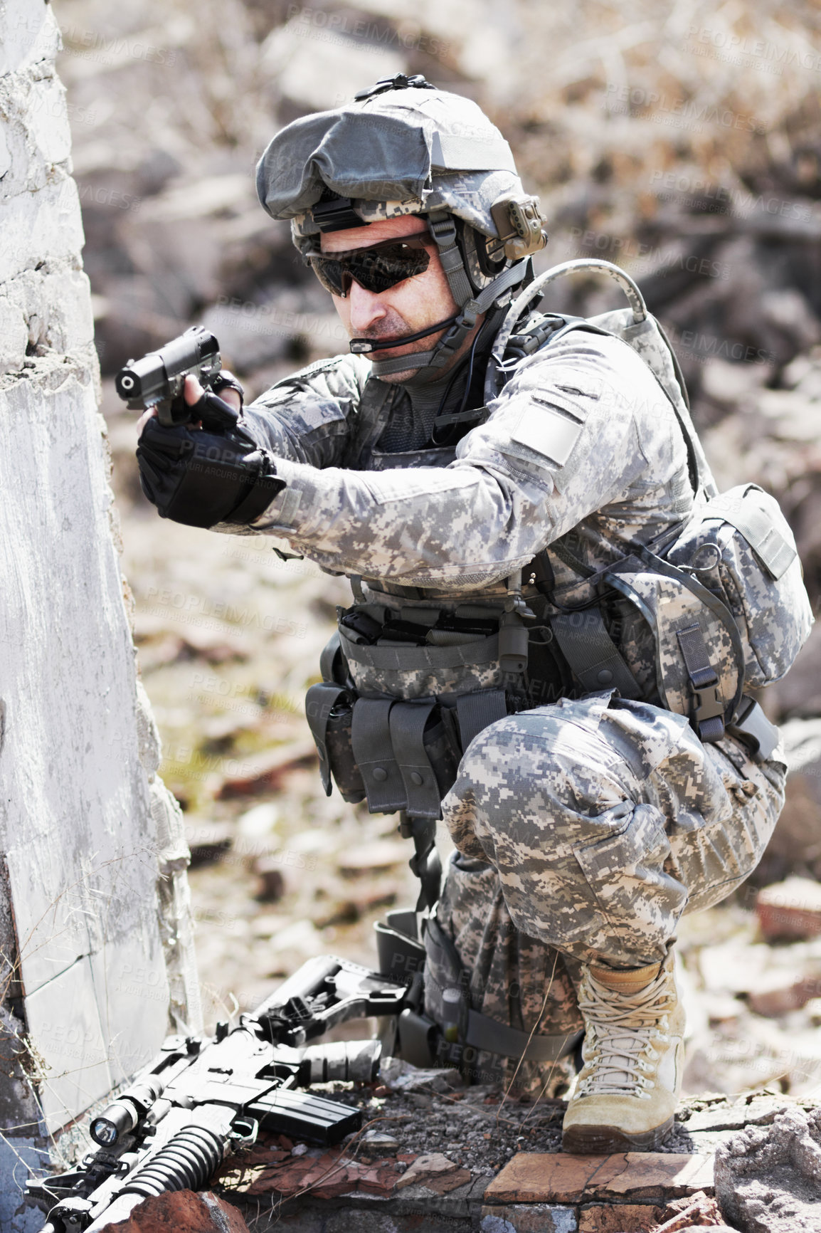 Buy stock photo A soldier crouched down next to a broken down wall and pointing his gun into the distance