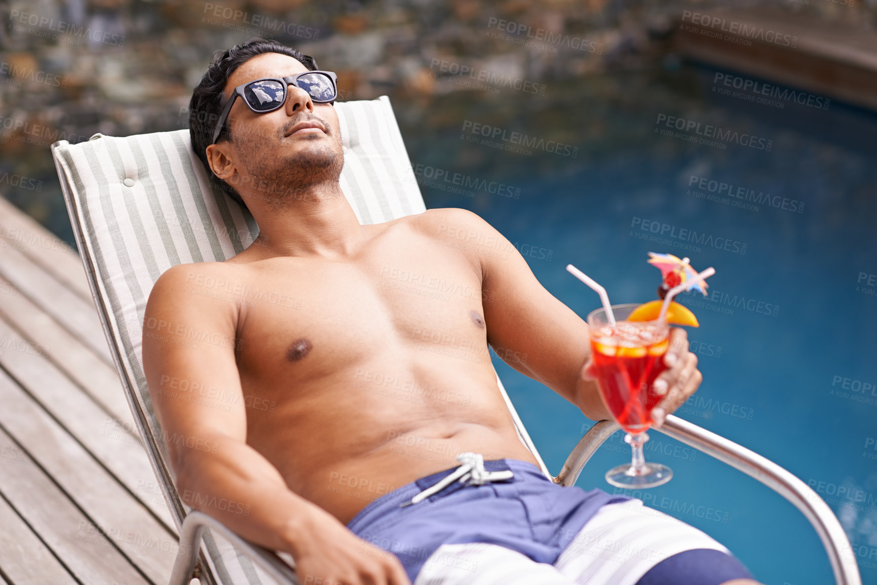 Buy stock photo Cropped shot of a man holding a cocktail while sitting in a deckchair beside a po